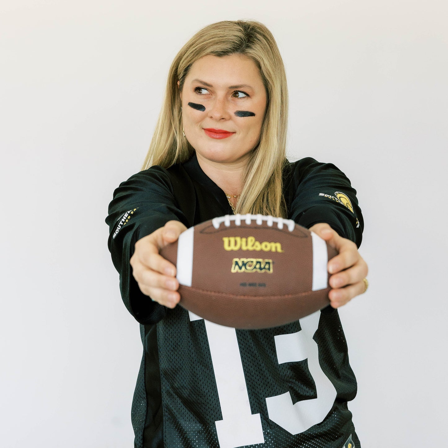Chae Carter of Carter's Collective Fine Jewelry in Hattiesburg, MS wearing a Southern Miss sports jersey holding a Wilson football against a white background