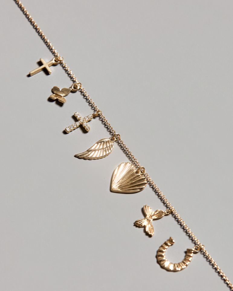 Gold necklace with various charms on a gray background